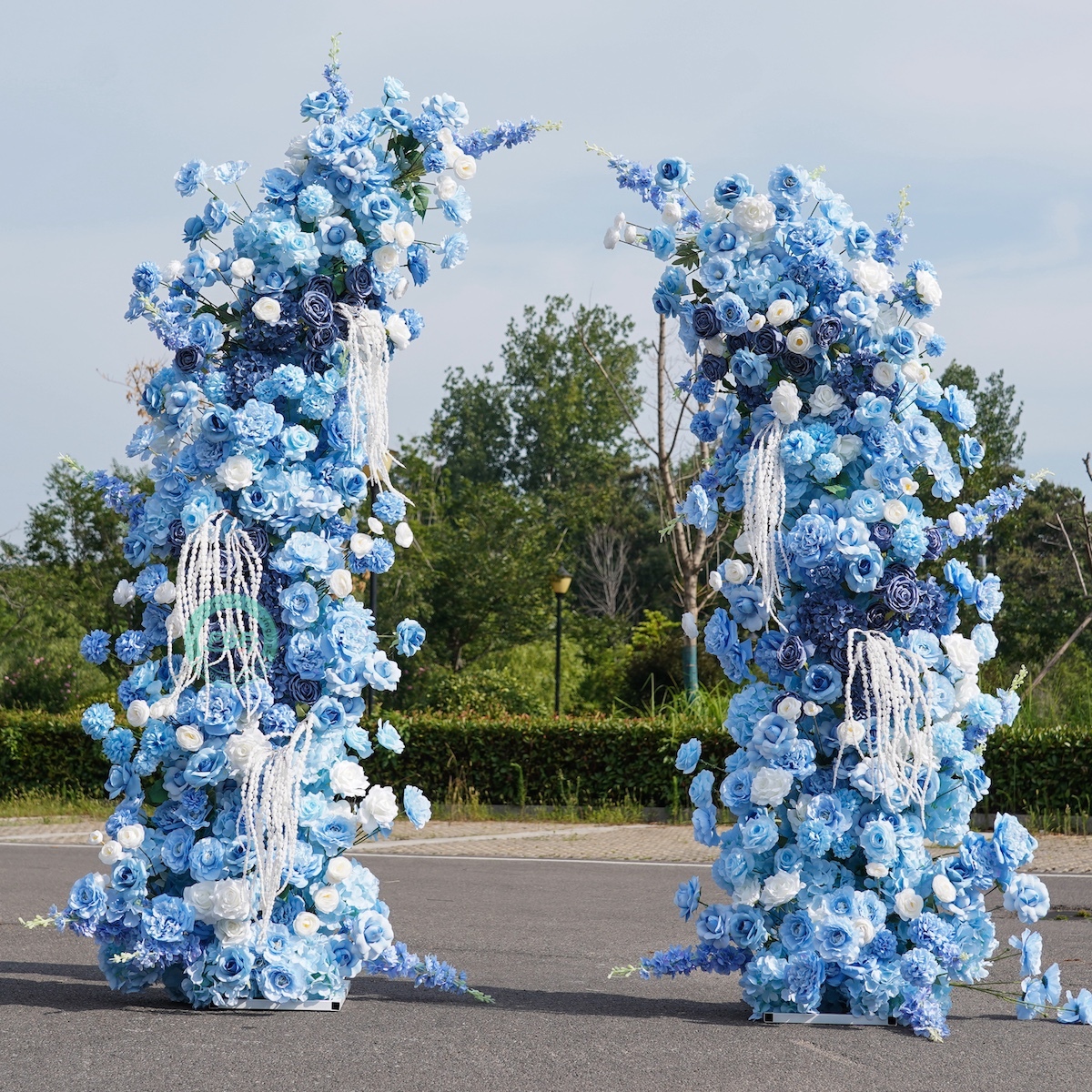 Front view of the 6.6ft x 7.2ft white horn wedding arch completely covered in full pre-attached blue and white artificial flowers with hanging tassels.